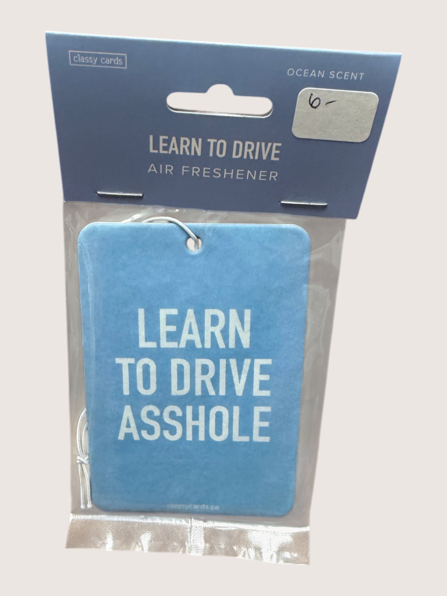 Blue air freshener with text 'LEARN TO DRIVE ASSHOLE' in packaging on a light gray background