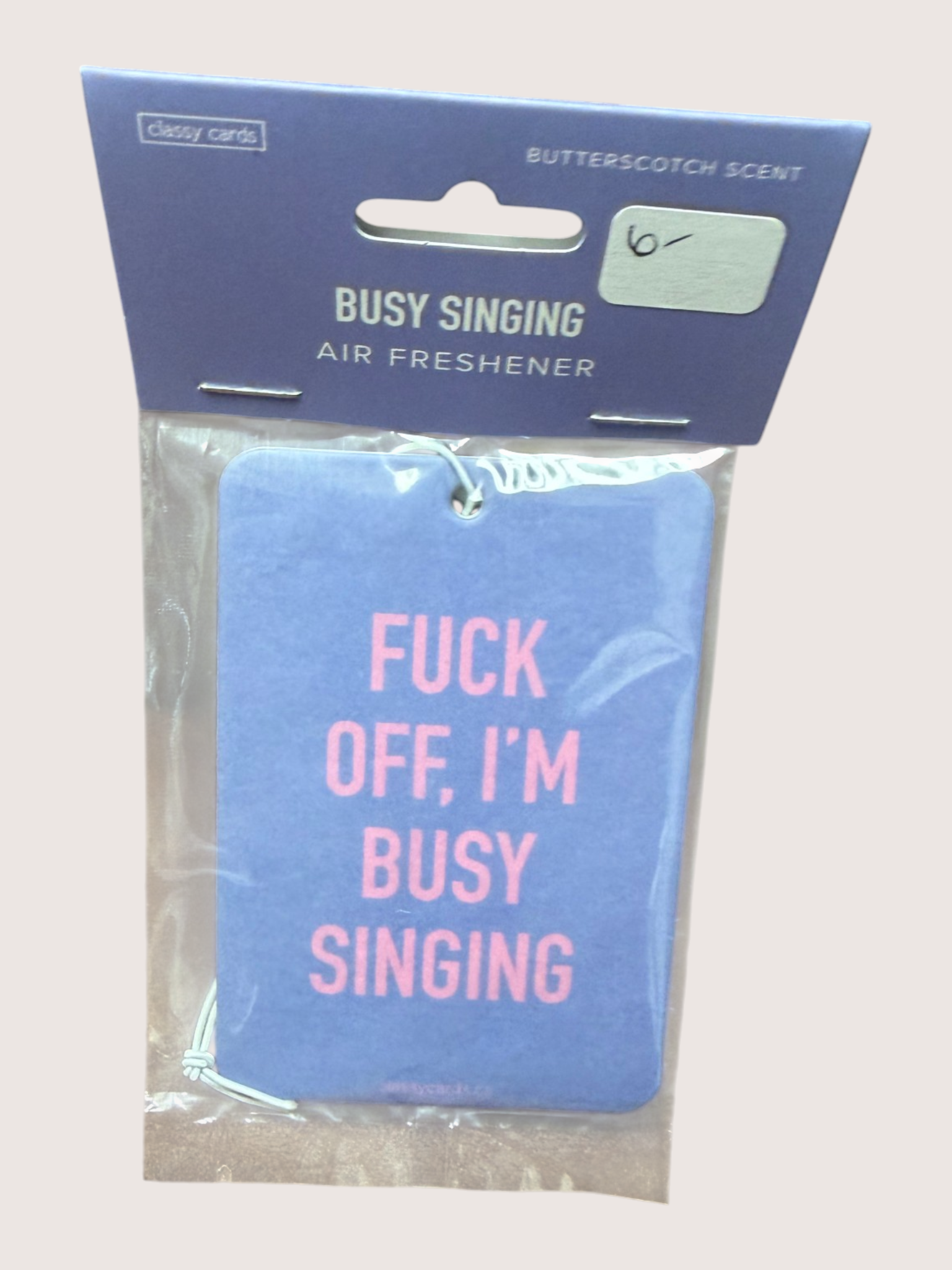Air freshener with text 'F*ck off, I'm busy singing' in pink on a blue background, packaged in clear plastic with a blue label.
