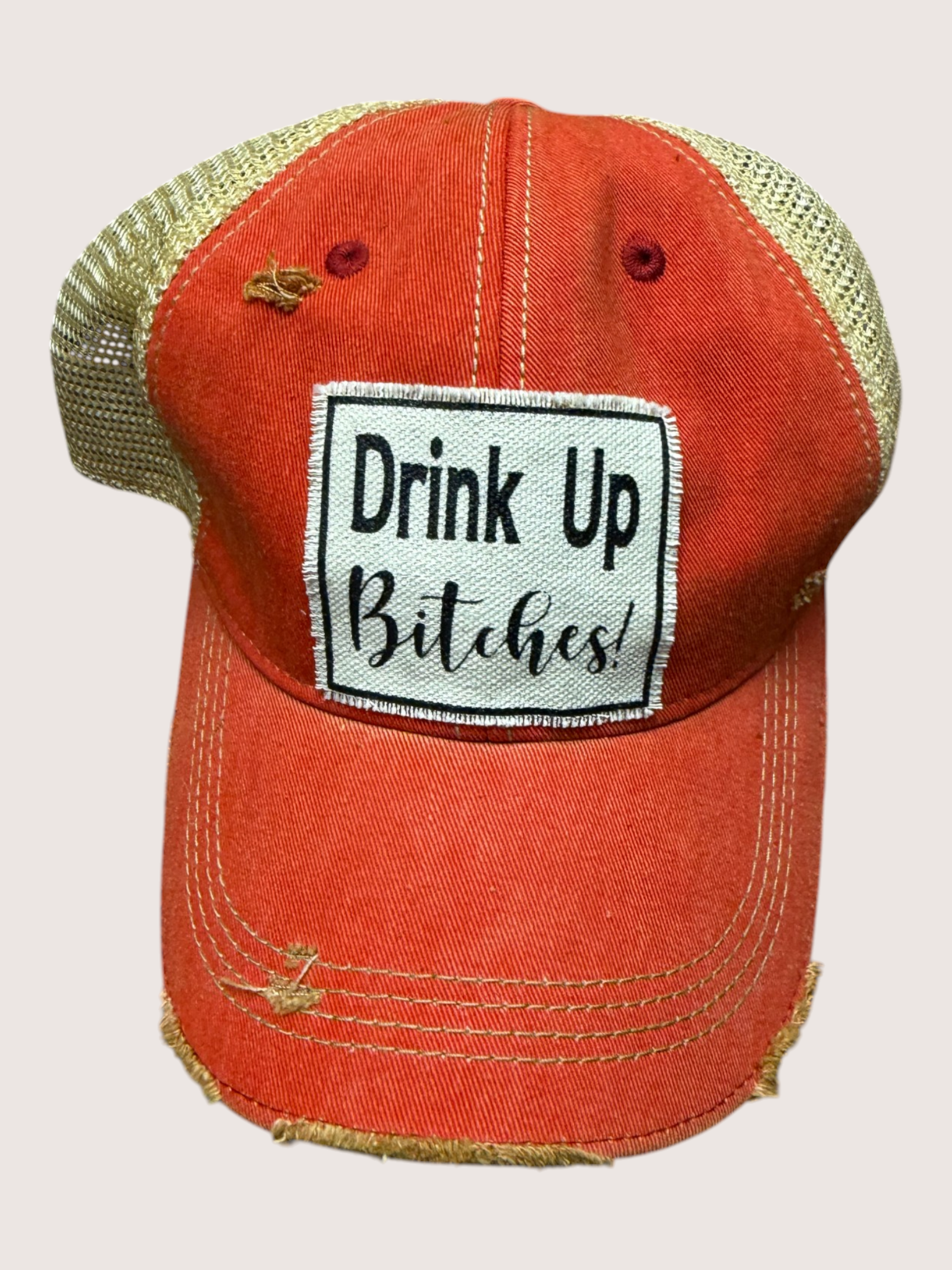 Red cap with 'Drink Up Bitches!' patch on a light pink background