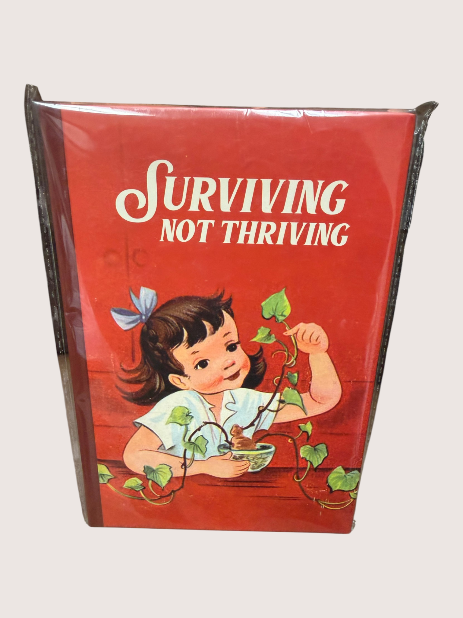 Vintage-style book with a child and text 'Surviving Not Thriving' on a red background.