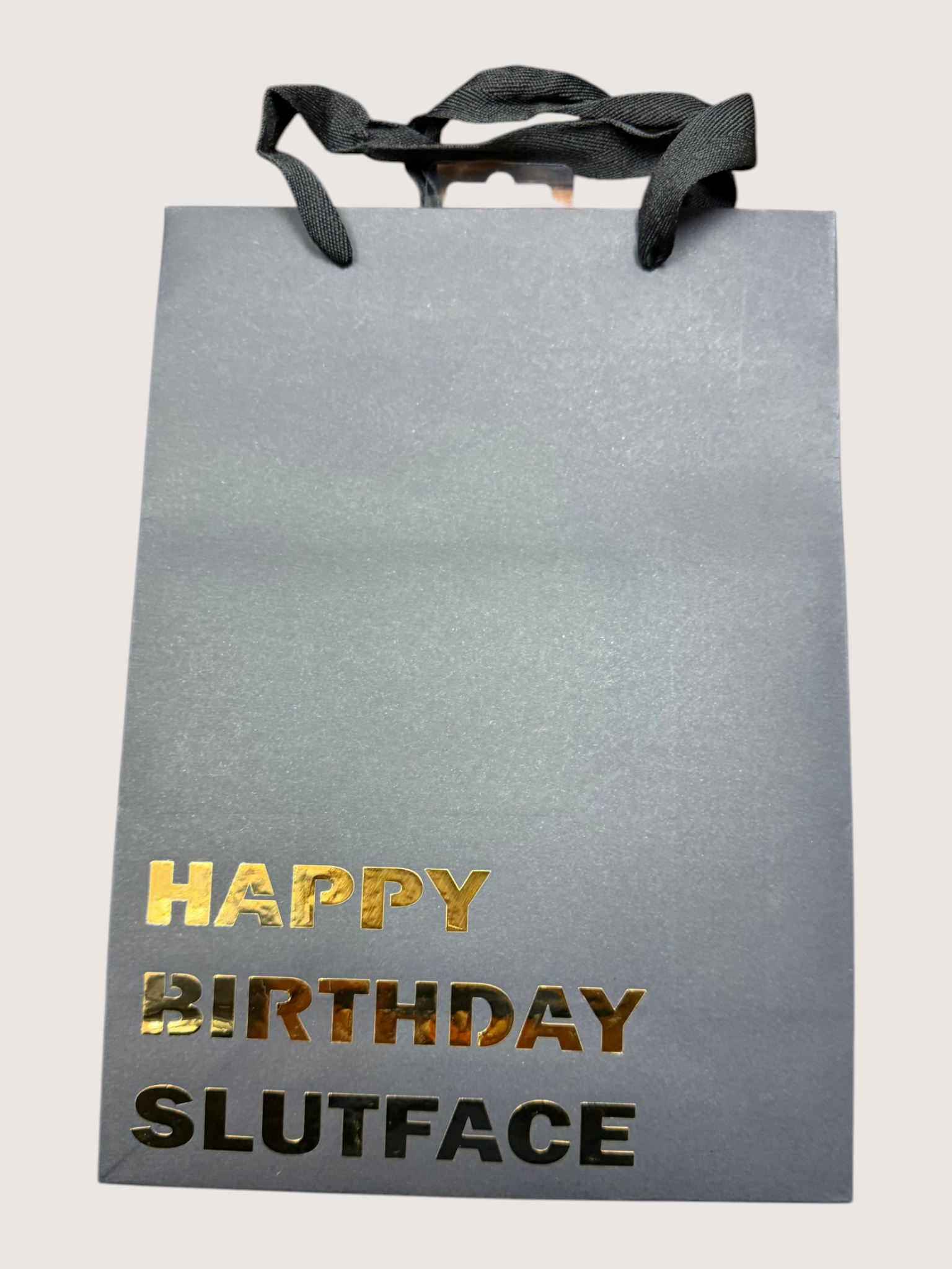 black gift bag with 'Happy Birthday Slutface' text in gold and black on a light gray background