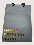 Black gift bag with 'Happy Birthday Bitch' text in gold on a white background
